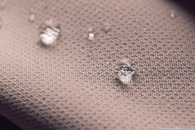 Nahaufnahme von wasserabweisendem Textilgewebe mit abperlenden Wassertropfen, basierend auf moderner Nanofasern-Technologie in funktionaler Arbeitskleidung
